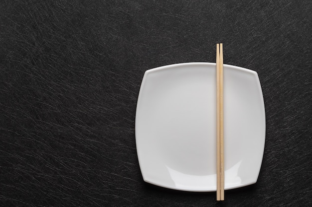 Assiette blanche vide avec des baguettes sur une table sombre. Style de cuisine japonaise. Vue de dessus