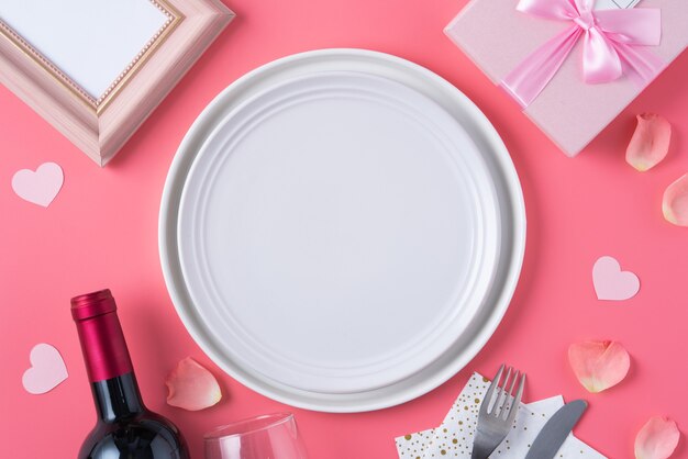 Assiette blanche vide avec cadeau et pétales de rose pour le concept de repas de rencontres spéciales Saint Valentin.