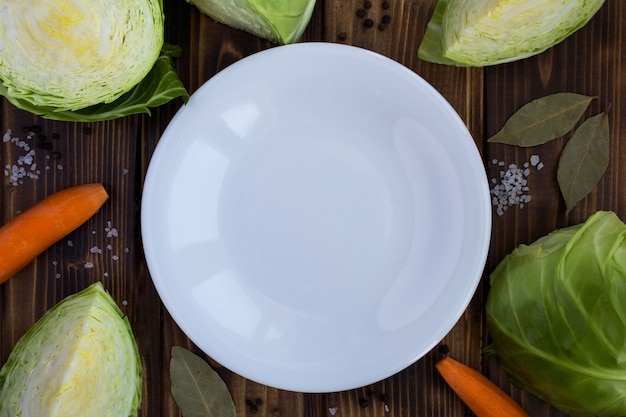 Assiette blanche vide, chou et carotte sur le fond en bois brun.Ingrédients alimentaires sains.Vue de dessus.Copier l'espace.