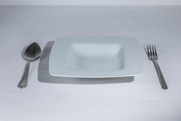 Une assiette blanche vide avec une cuillère et une fourchette. Fond clair