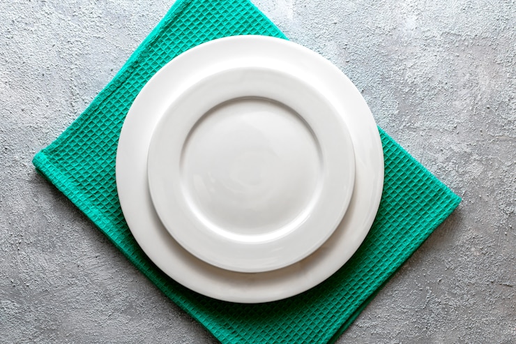 Photo assiette blanche vide servi sur une serviette en relief et fond de béton gris en relief. vue de dessus maquette pour le menu