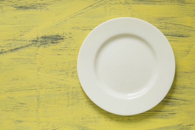 Assiette blanche vide sur une surface en bois peinte jaune. Vue d&#39;en-haut. Copier l&#39;espace