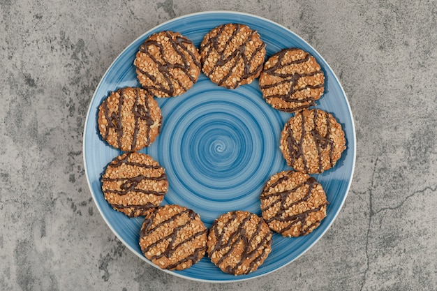 Assiette bleue de biscuits aux graines et chocolat sur marbre.