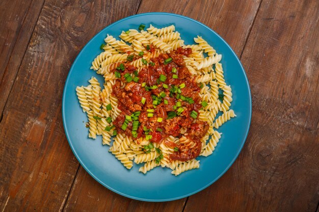 Assiette bleue avec des pâtes bolognaises sur une table en bois saupoudrée d'oignons