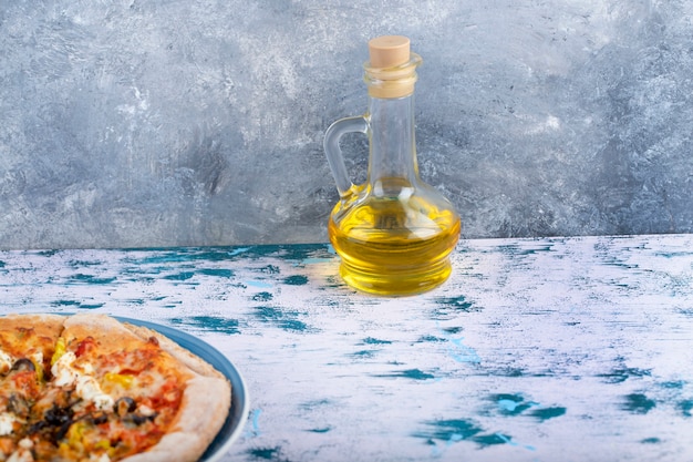 Assiette bleue de pizza au fromage et verre d'huile sur table en marbre.