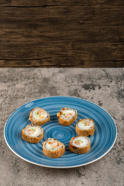 Assiette bleue de rouleaux de tempura placés sur une surface en pierre.