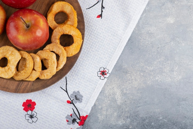 Assiette en bois d'anneaux de pomme séchée et pomme rouge sur nappe blanche.