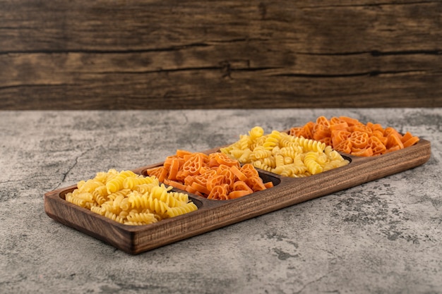 Assiette en bois de diverses pâtes crues sur table en pierre.