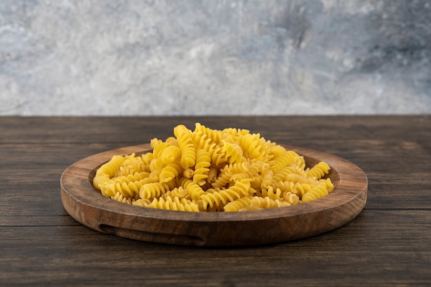 Assiette en bois de pâtes fusilli non cuites sur une surface en bois.