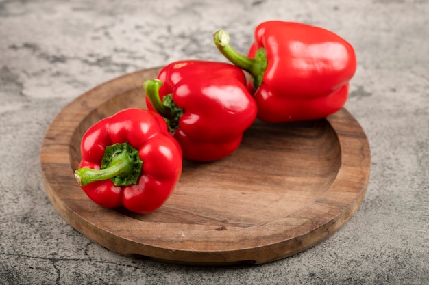 Assiette en bois et poivrons rouges mûrs sur la surface de la pierre