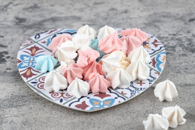 Assiette de bonbons meringués sucrés colorés sur fond de pierre.