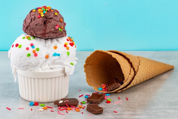 Assiette de boules de glace à la vanille et au chocolat avec saupoudres de morceaux de chocolat et cornets gaufres sur fond bleu.