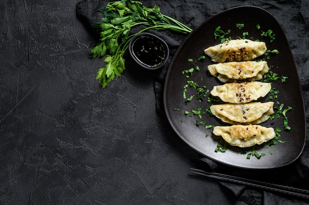 Assiette de boulettes de gyoza japonais frites sur table noire rustique.