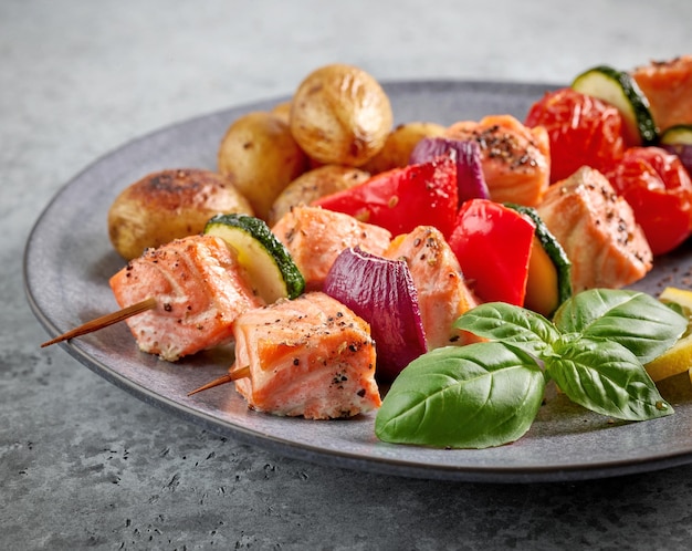 Assiette de brochettes de saumon grillé et légumes sur table grise close up