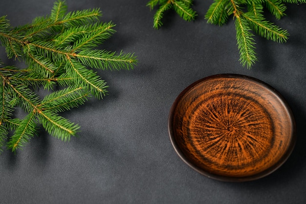 Une assiette brun orangé et des branches d'arbre de Noël vert se trouvent sur fond gris vue d'en haut