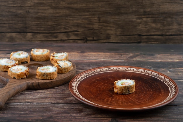 Assiette brune de délicieux rouleaux de tempura sur une surface en bois.