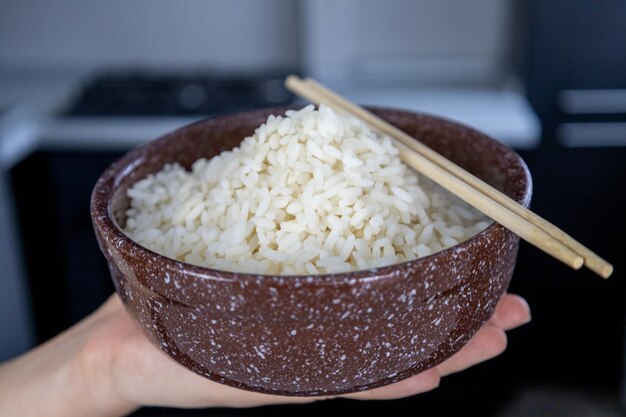 Une assiette brune avec du riz doré dans la paume de la main d'une fille dans la cuisine Concept de cuisine asiatique