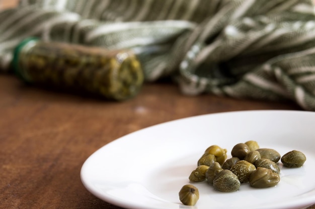 Assiette avec câpres et verre couché avec câpres marinées à côté d'un tissu rayé vert