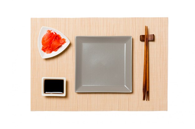 Assiette carrée grise vide avec des baguettes pour sushi, gingembre et sauce soja sur tapis de sushi brun