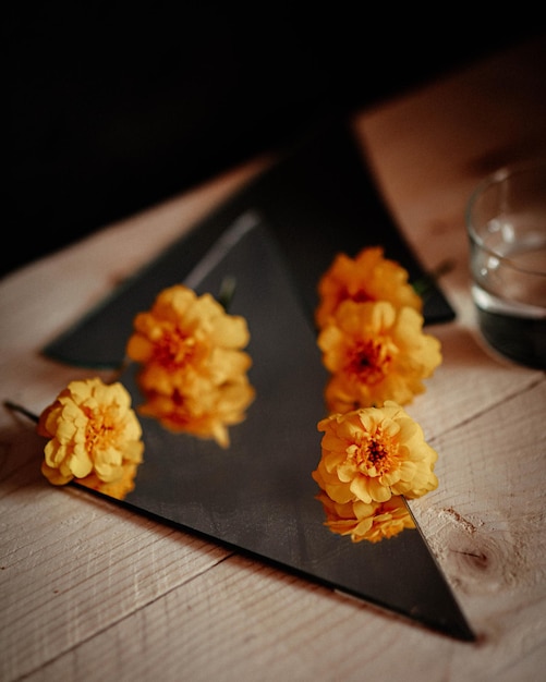 Une assiette carrée noire avec trois fleurs jaunes dessus.