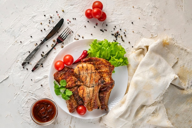 Assiette en céramique blanche avec bœuf de porc grillé, feuilles de laitue, tomate et piment rouge et sauce dans les bols