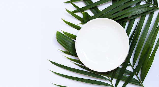 Une assiette en céramique blanche vide sur des feuilles de palmier tropical