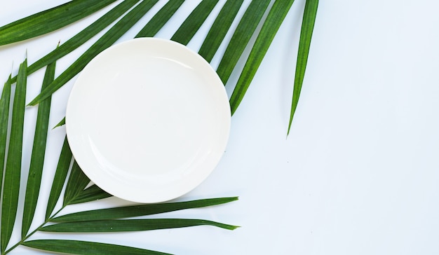 Une assiette en céramique blanche vide sur des feuilles de palmier tropical