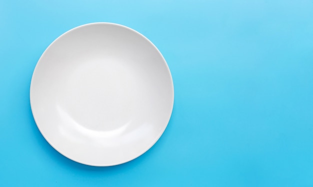 Assiette en céramique blanche vide sur fond bleu.