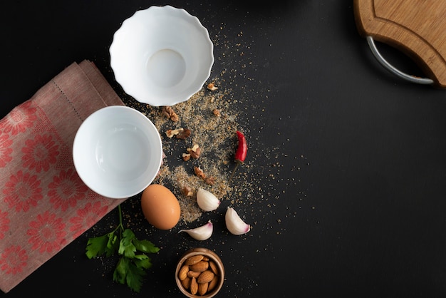 Assiette en céramique blanche vide sur la table noire, ingrédients frais pour la cuisson, poivre moulu, vaisselle