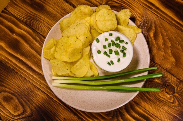 Assiette en céramique avec croustilles et bol en verre avec crème sure sur table en bois Vue de dessus