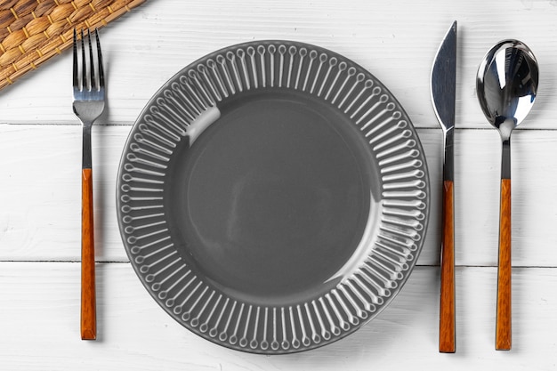 Assiette en céramique gris brillant avec des couverts sur une table de cuisine en bois