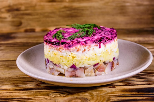 Assiette en céramique avec hareng salade traditionnelle russe du nouvel an sous manteau de fourrure (shuba) et sur table en bois rustique