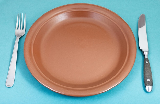 Assiette en céramique marron avec fourchette et couteau sur vert