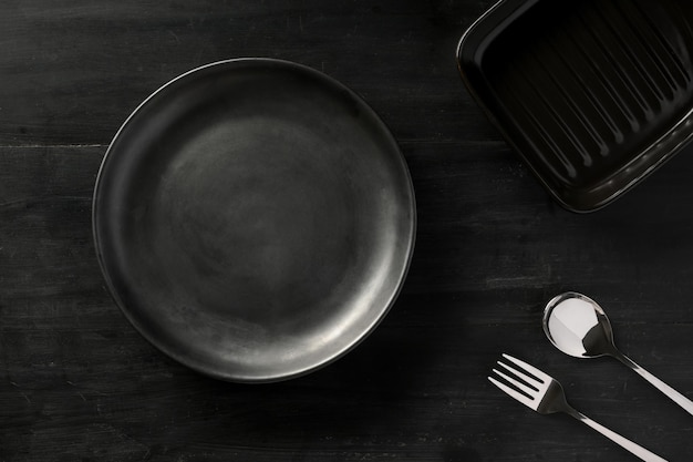 Assiette en céramique noire vide avec de l'argenterie sur l'image de vue de dessus de fond de table à manger noire