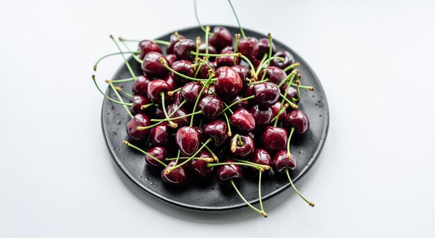 Assiette de cerises douces fraîches avec des feuilles dans des gouttes d'eau sur la vue de dessus de fond de pierre