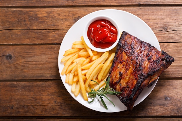 Assiette de côtes de porc grillées avec frites sur table en bois, vue du dessus