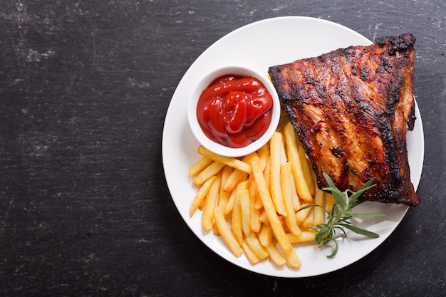 Assiette de côtes de porc grillées avec frites sur table sombre, vue du dessus