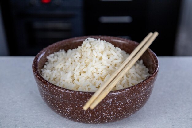 Une assiette de couleur marron avec du riz doré et des baguettes sur la table dans le contexte d'un concept de cuisine asiatique de cuisine sombre