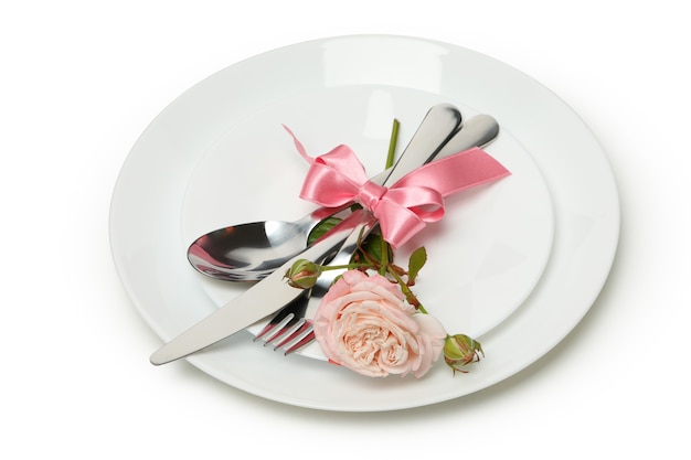 Assiette avec couverts, noeud rose et rose isolé sur fond blanc