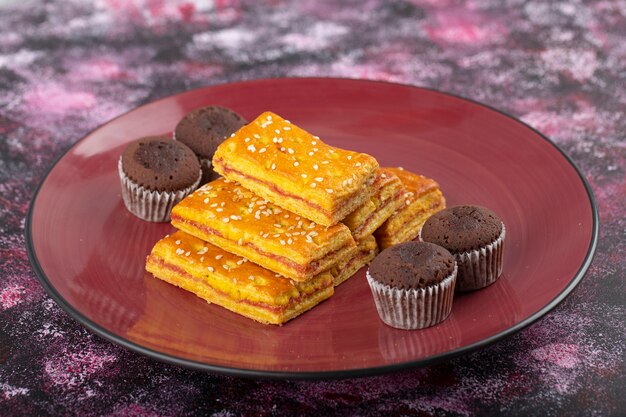 Assiette de craquelins sucrés et muffins au chocolat placés sur une table colorée.