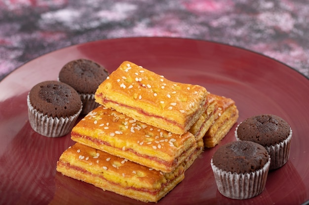 Assiette de craquelins sucrés et muffins au chocolat placés sur une table colorée.