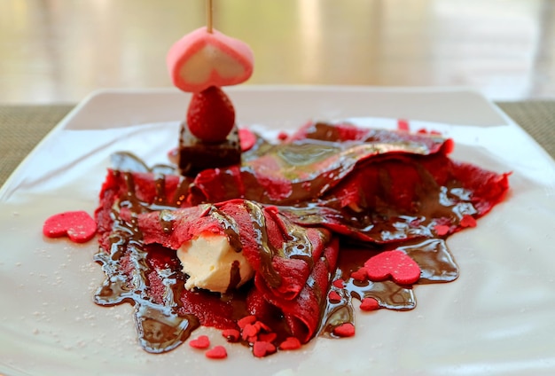 Assiette de crêpe rouge framboise avec sauce au chocolat et bonbons en forme de coeur rose