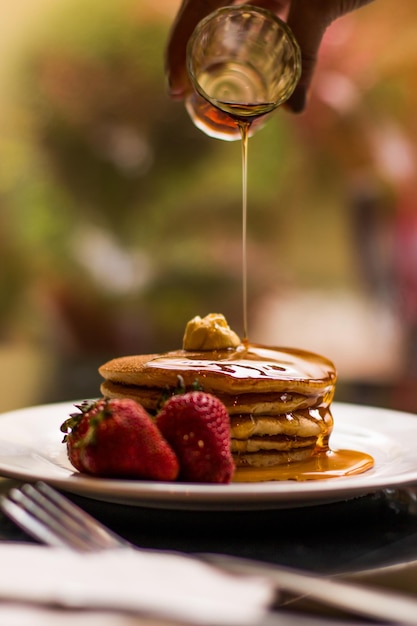 Assiette de crêpes avec fraises fraîches, beurre et miel, érable et sirop tombant dessus