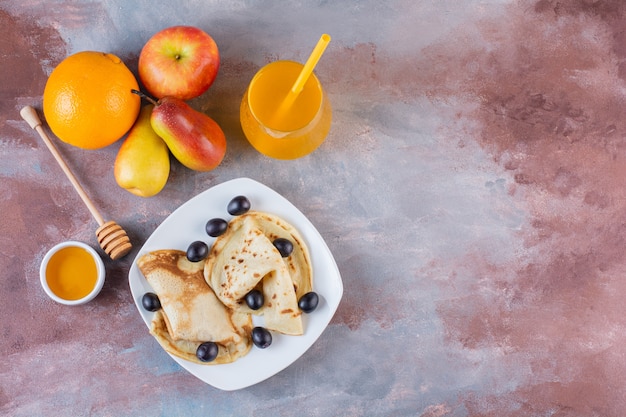 Assiette de crêpes avec verre de jus de fruits frais sur table en marbre.