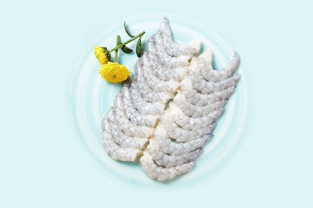 Une assiette de crevettes crues avec une assiette bleue sur fond blanc