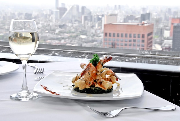 assiette de crevettes rôties au beurre verre de vin blanc, table de restaurant, vue panoramique sur la ville, nourriture