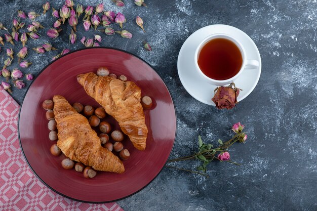 Assiette de croissants aux noisettes et tasse de thé noir sur marbre.