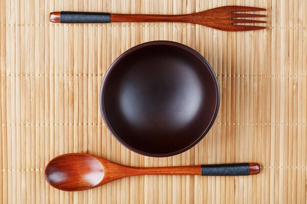 Assiette, cuillère et fourchette en bois naturel sur un support en bambou.