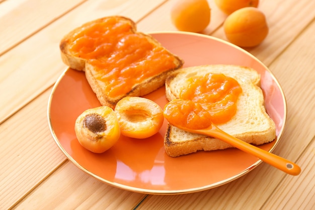 Assiette avec de délicieuses tranches de pain et confiture sur table en bois