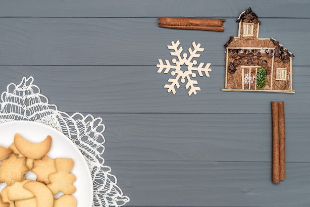 Assiette avec de délicieux biscuits de Noël à la cannelle et flocon de neige décoratif et maison sur table en bois